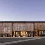 Exterior view of the Center for Wooden Boats, featuring a charming waterfront building with a rustic wooden facade and large windows. The structure is surrounded by boats on the water, with a backdrop of trees and a clear sky. The scene captures the vibrant atmosphere of the center, which serves as a hub for maritime education and community engagement in boating activities.